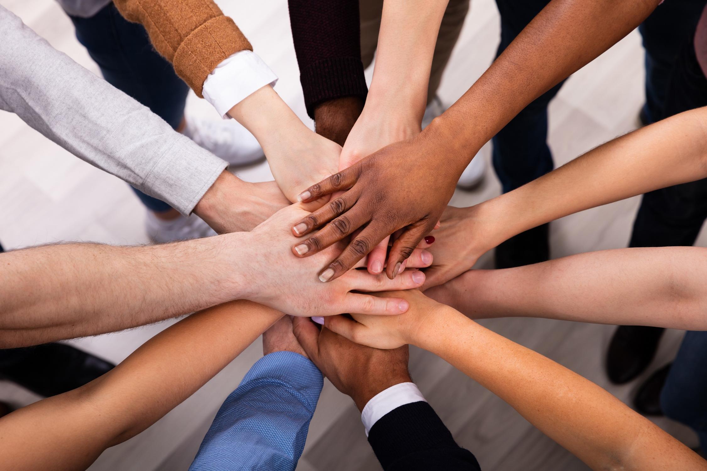 Viele diverse Personen halten ihre Hände in die Mitte.